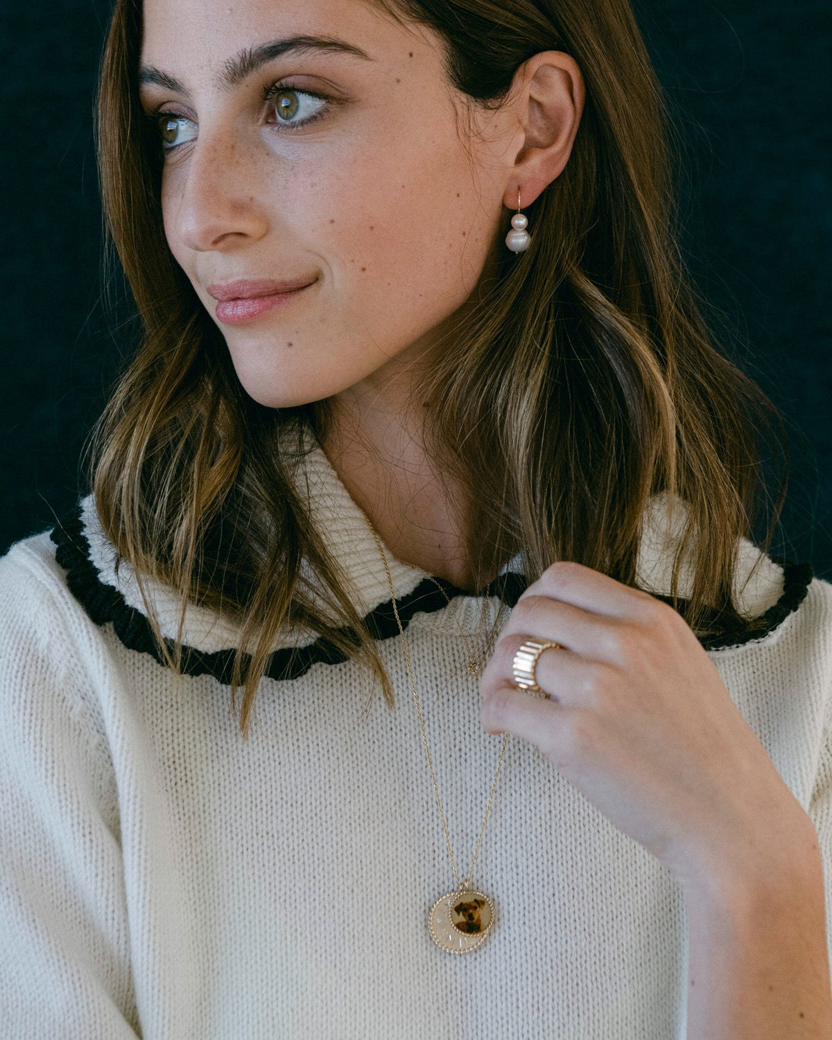 Imperial Portrait Pendant with a dog portrait on a model in a cream knit sweater, her hands at her collar.