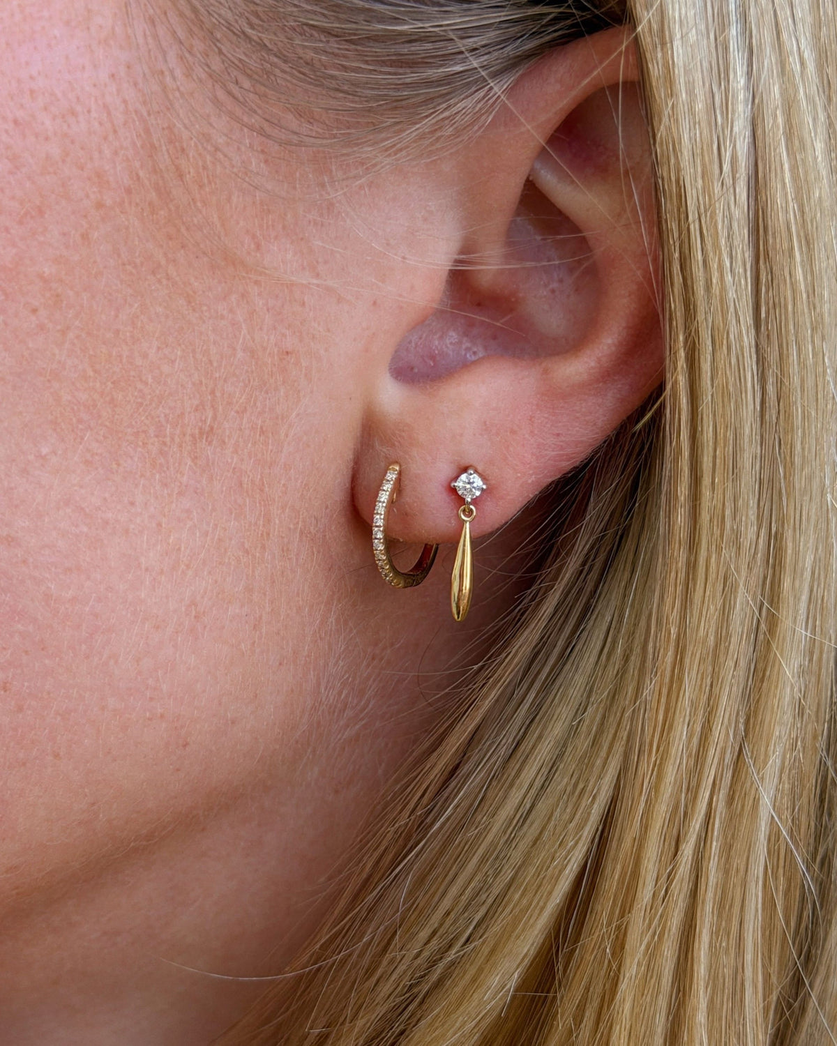 Pave Diamond Huggie in a close-up ear stack beside a diamond stud with a gold spike drop, blonde hair behind.