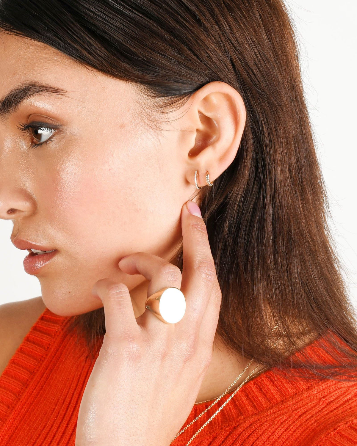 Pave Diamond Huggies in two lobe piercings of a model in an orange knit top, fingertip at her jaw.