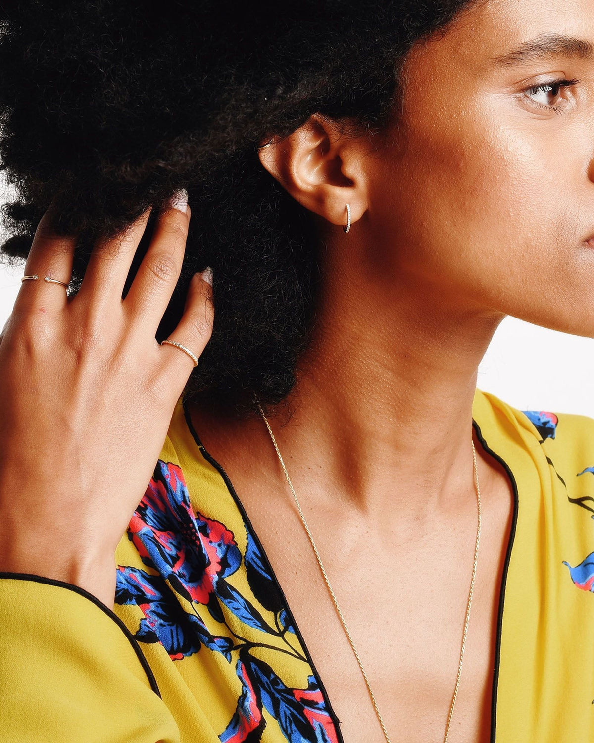 Pave Diamond Huggie on a model with curly hair in a yellow floral blouse, her hand lifting her hair.