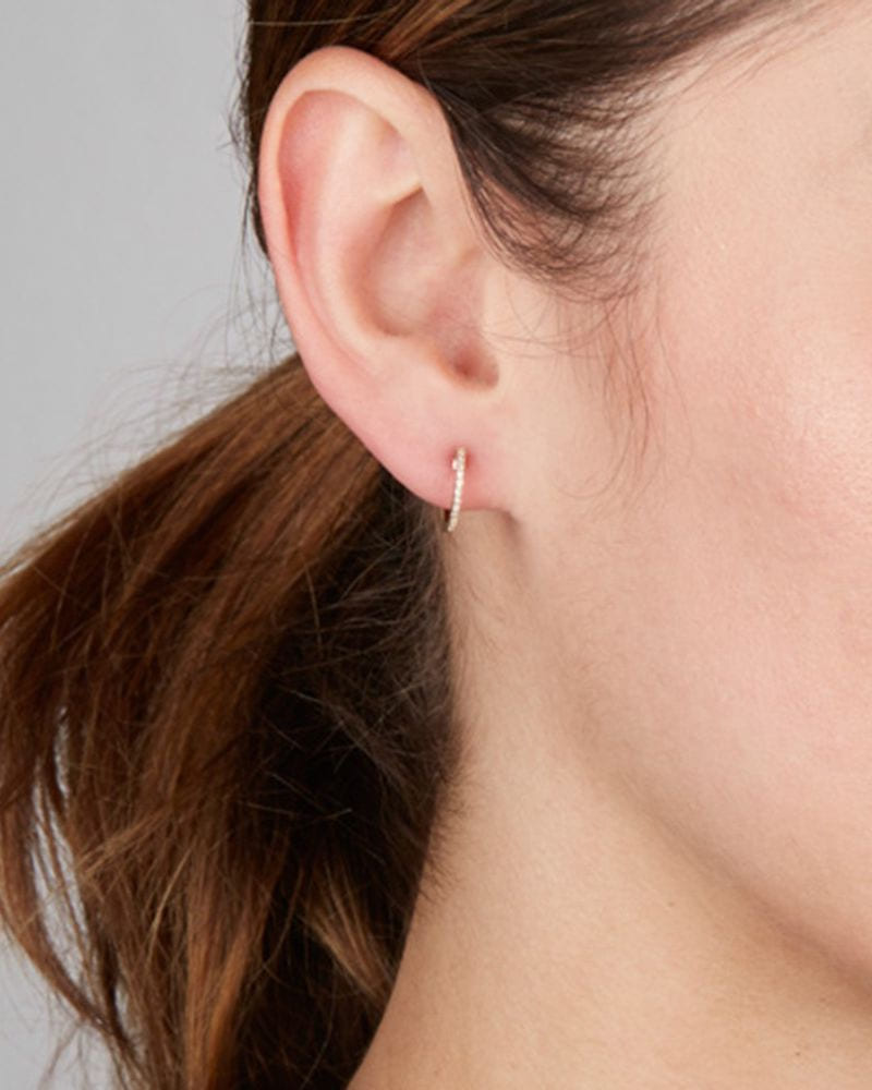 Pave Diamond Huggie in close-up on the ear of a model with a low brown ponytail.
