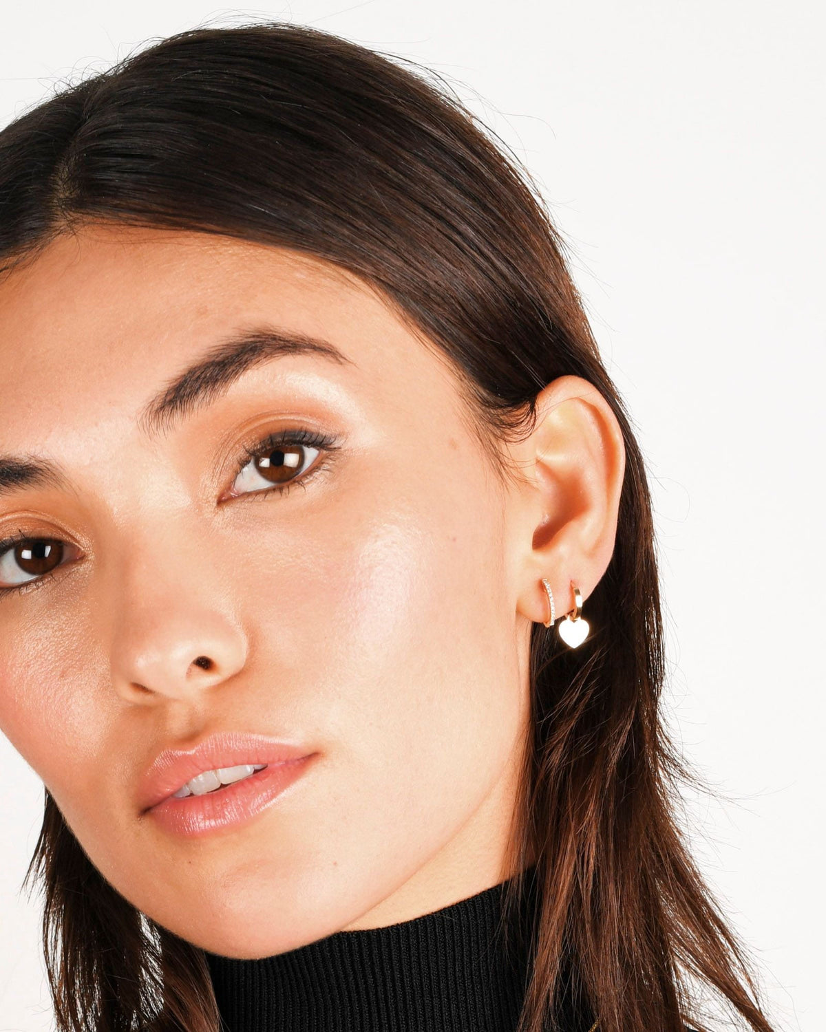Pave Diamond Huggie on a model in a black turtleneck, beside a gold heart charm huggie.