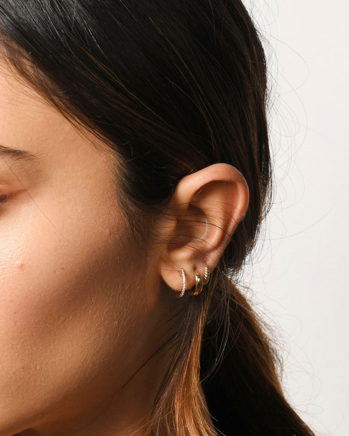 Pave Diamond Huggie in an ear stack with gold huggies on a model with a long ponytail.