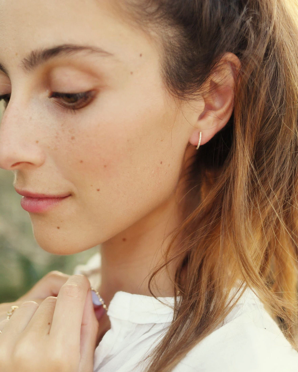 Pave Diamond Huggie on a model in a white shirt in golden outdoor light, fingertips at her collar.