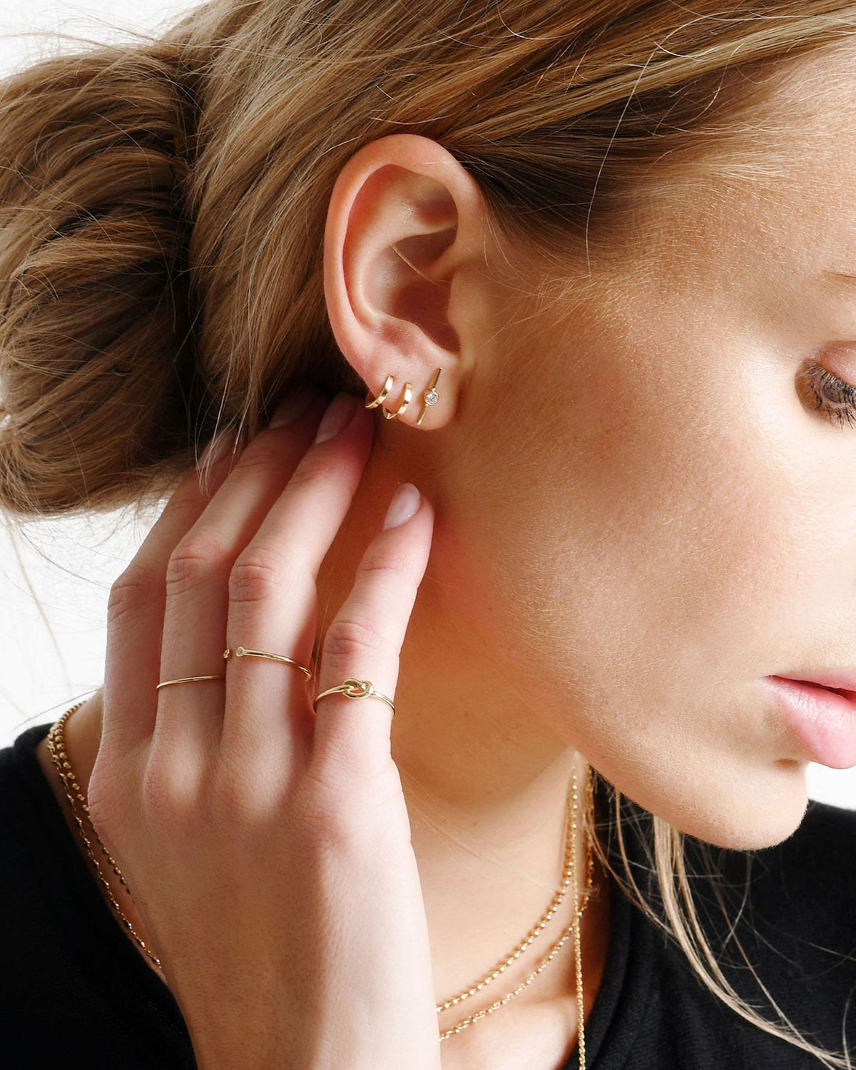 Petite Hoops in an ear stack with a diamond stud on a model with a messy bun, her hand at her neck.