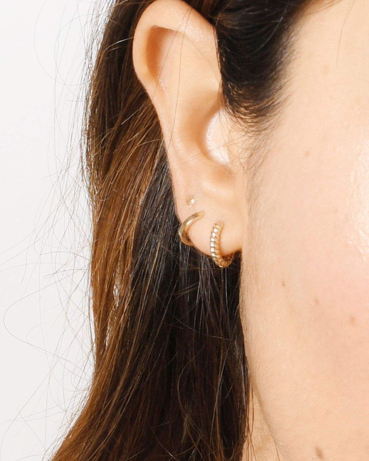 Petite Hoop in a close-up ear stack with a twisted hoop and a tiny stud on a model with brown hair.