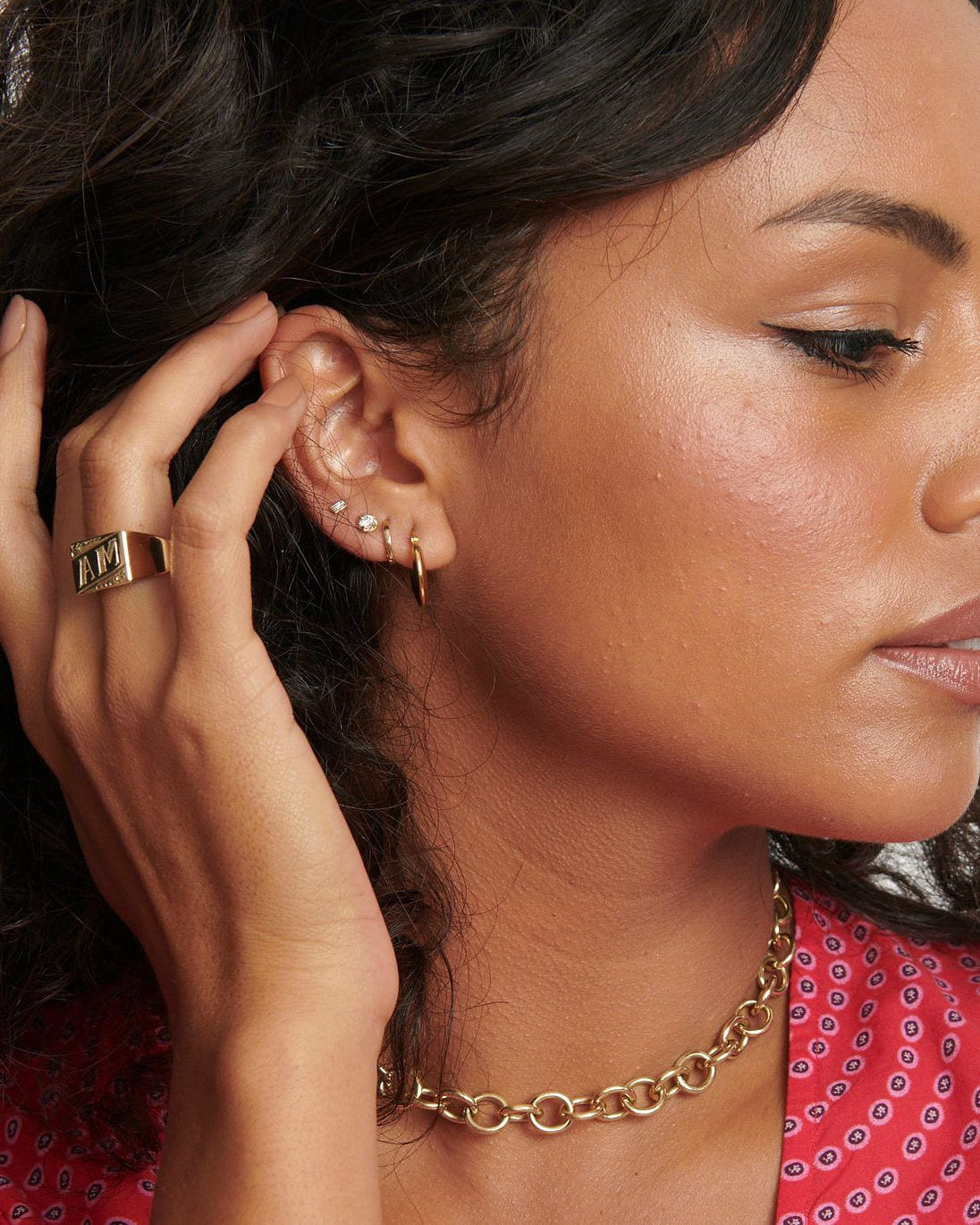 Petite Hoop at the end of an ear stack of diamond studs on a model with curly hair, hand at her ear.