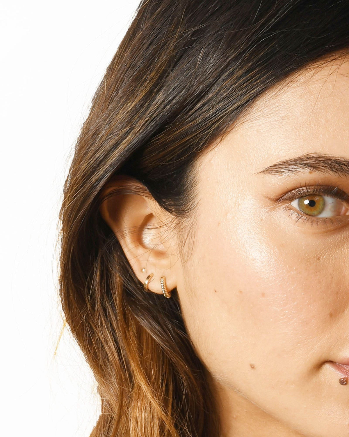 Petite Hoop with a twisted hoop and a tiny stud on a model with long ombre hair, her eye in view.