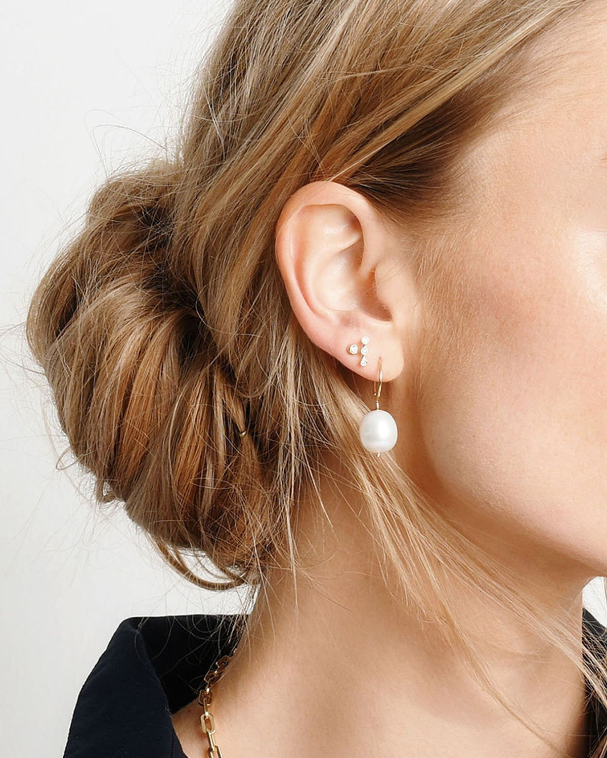 Baroque Pearl Swing Hoop on the ear of a model with a low messy bun, worn with a small diamond stud.
