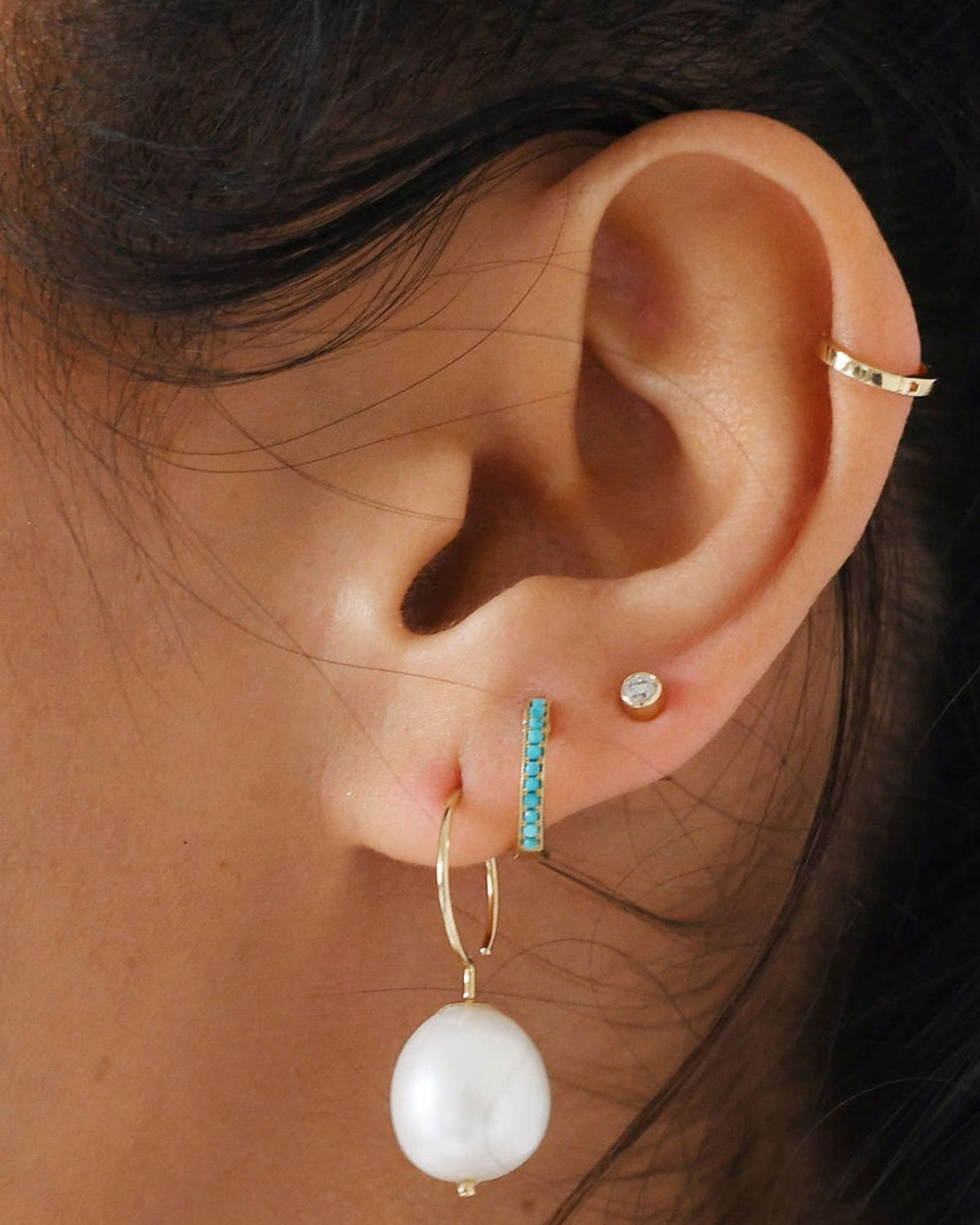 Baroque Pearl Swing Hoop in a close-up ear stack with a turquoise huggie, a diamond stud and a gold cuff.