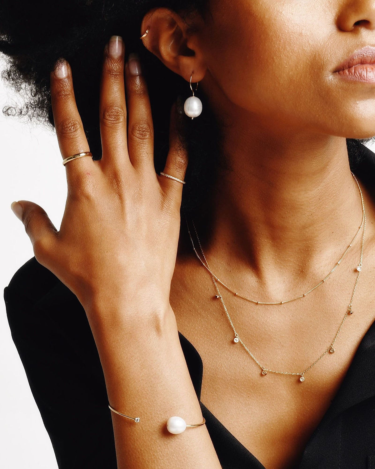 Baroque Pearl Swing Hoop on a model in a black blazer, her hand at her ear and a pearl cuff on her wrist.
