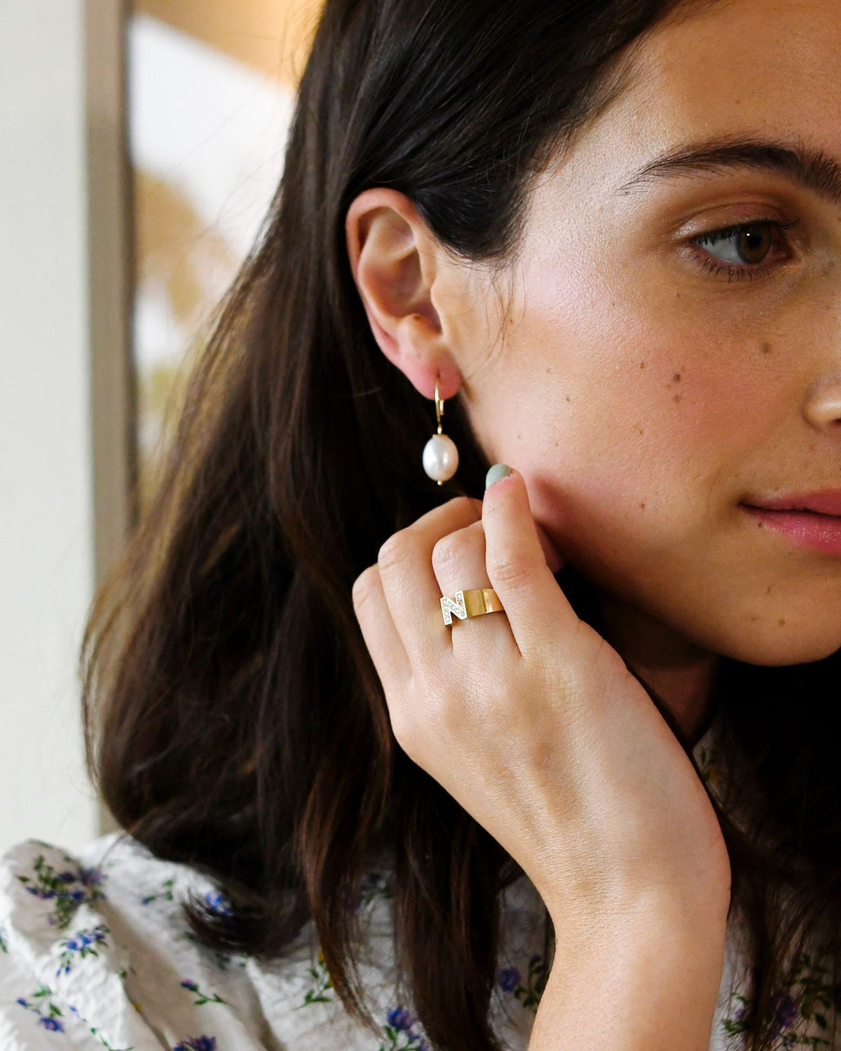 Baroque Pearl Swing Hoop on a dark-haired model in a floral blouse, fingertips touching her jaw.