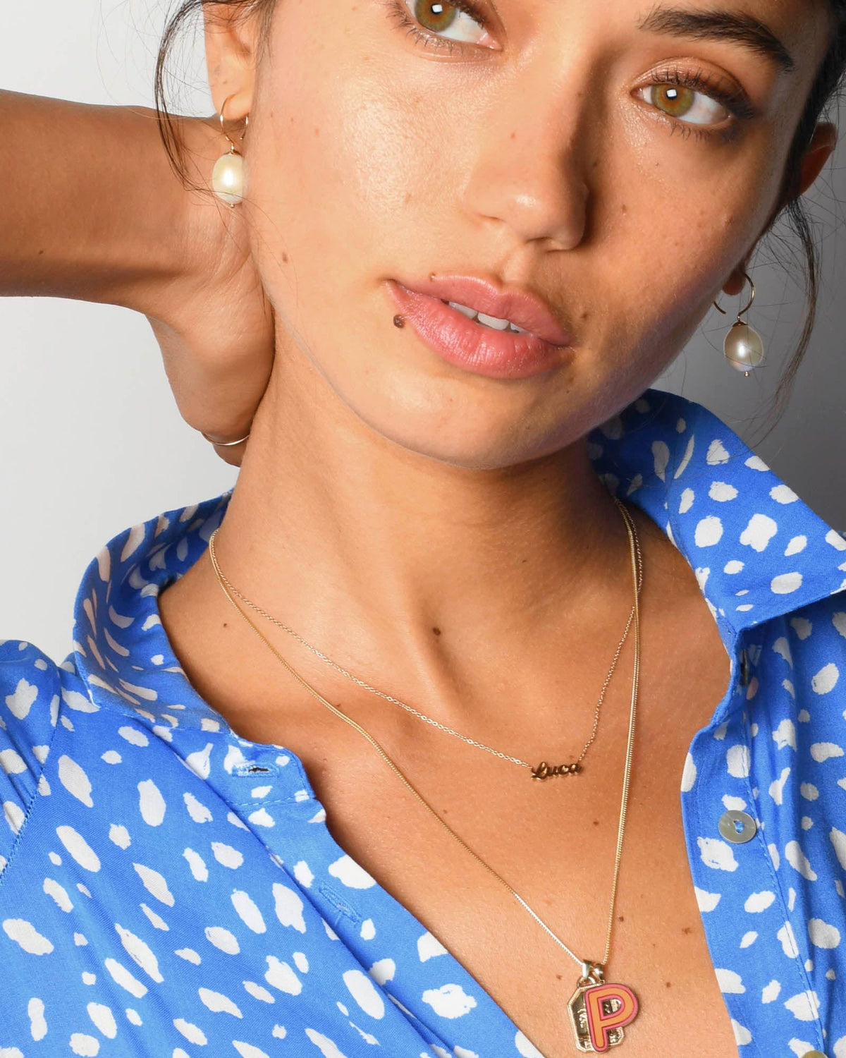 Baroque Pearl Swing Hoops on both ears of a model in a blue spotted shirt, one hand behind her neck.