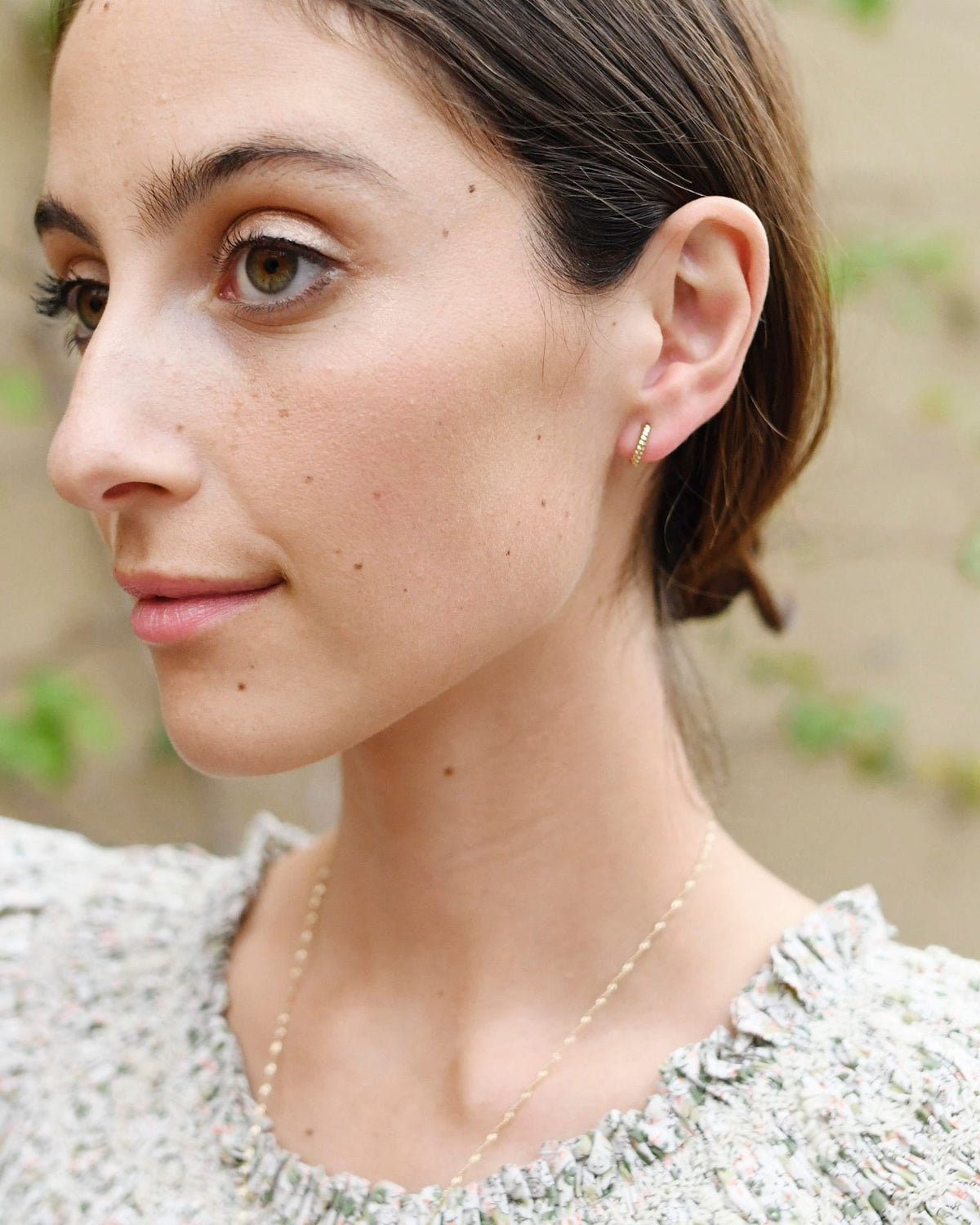 Twisted Petite Hoop on the ear of a model in profile with slicked-back hair and a floral ruffle top.