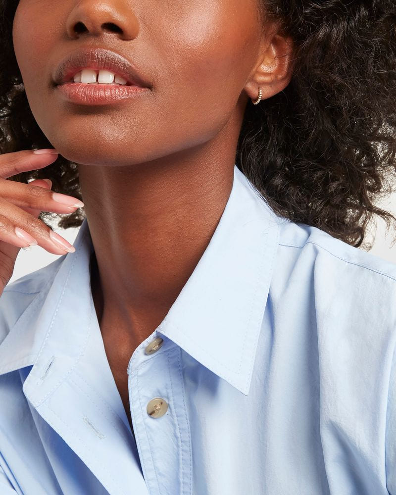 Twisted Petite Hoop on a model with curly hair in a light blue shirt, her fingertips at her chin.
