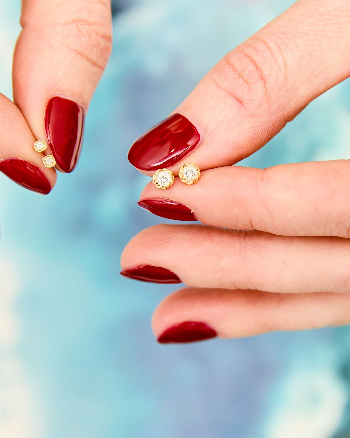 Diamond Twine Studs held between red-manicured fingertips against a soft blue background.