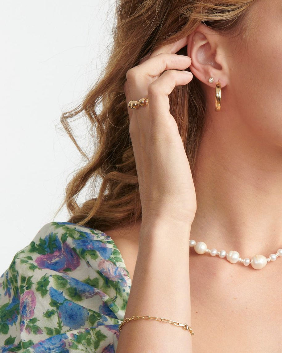 Diamond Twine Stud above a gold hoop on a model touching her ear, with a pearl necklace and floral sleeve.