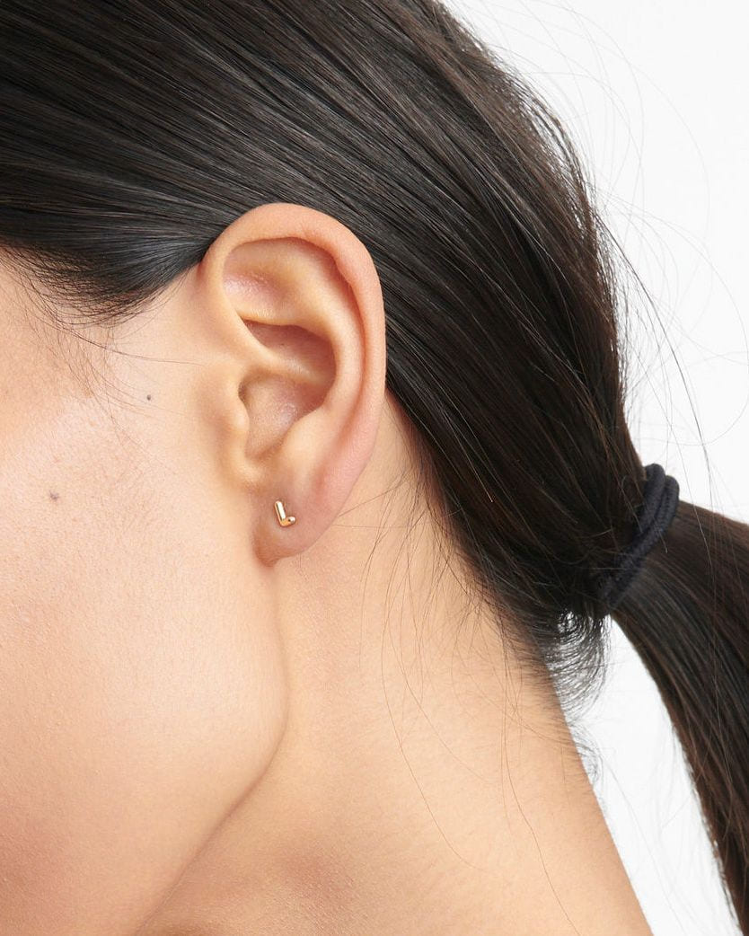 Mini Helium Initial Stud in the letter L on the bare ear of a model with a low dark ponytail.