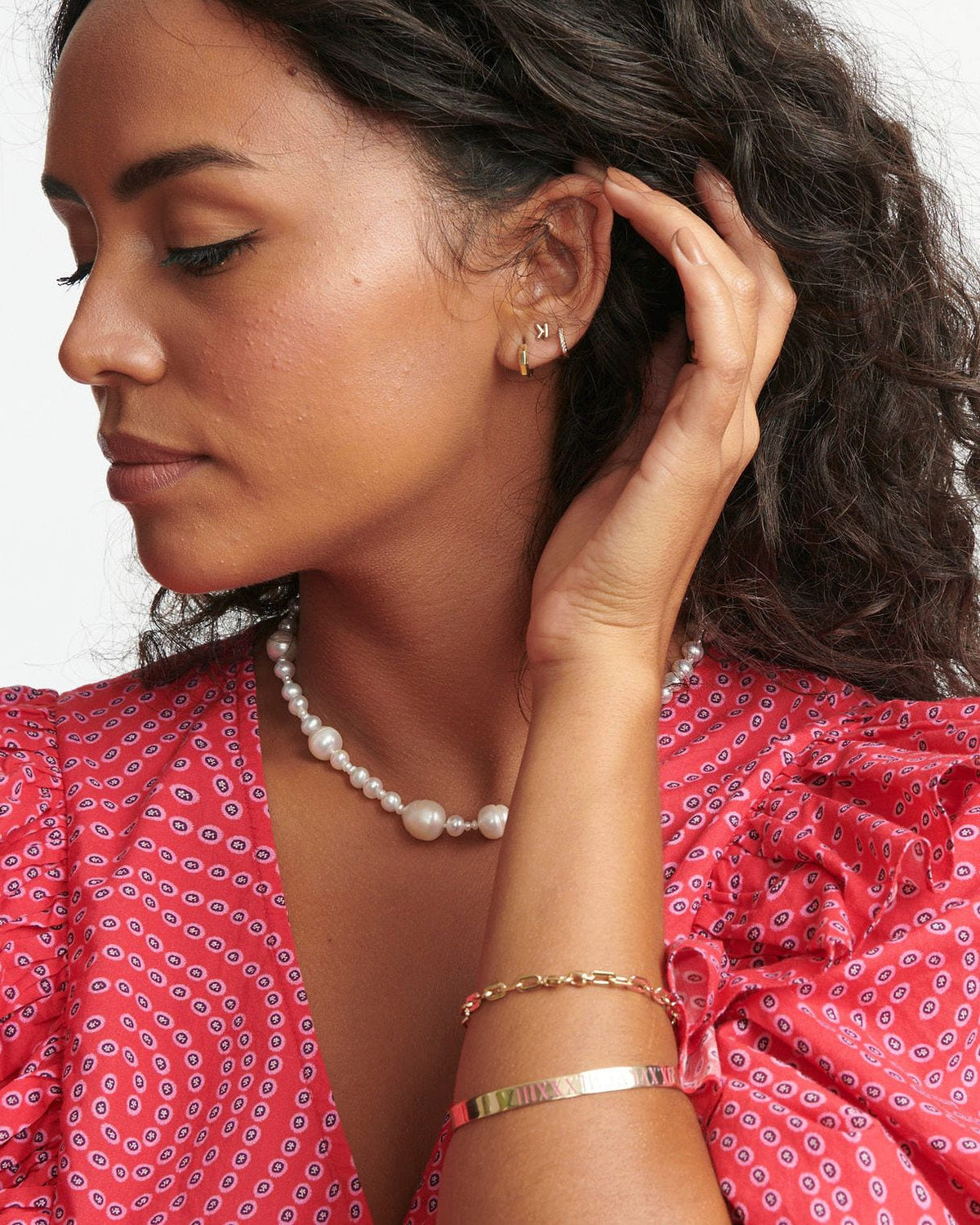 Mini Helium Initial Stud in the letter K in an ear stack, model touching her curls in a red print blouse.