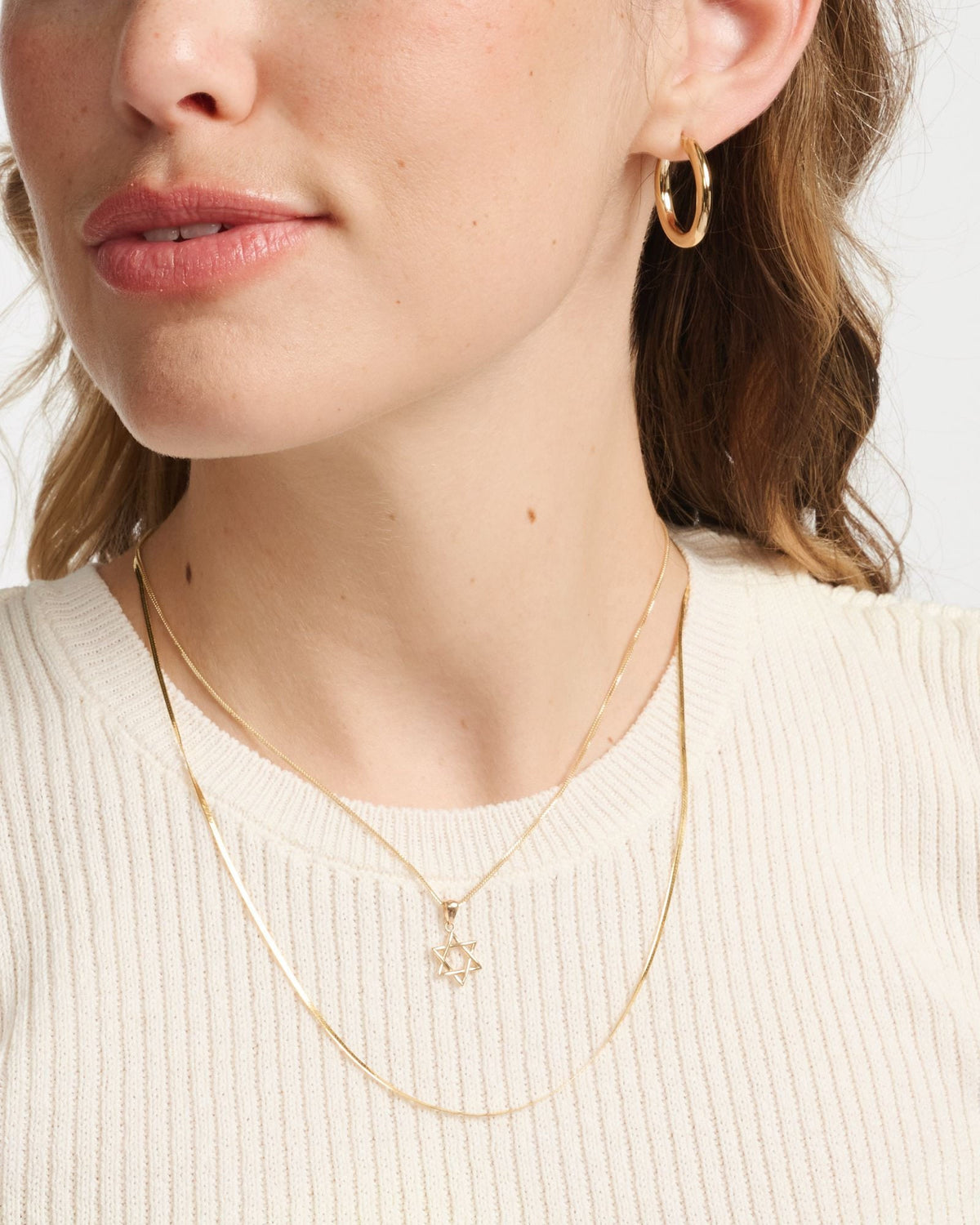 Junior Helium Hoop on a model in a cream ribbed tee with a Star of David necklace.