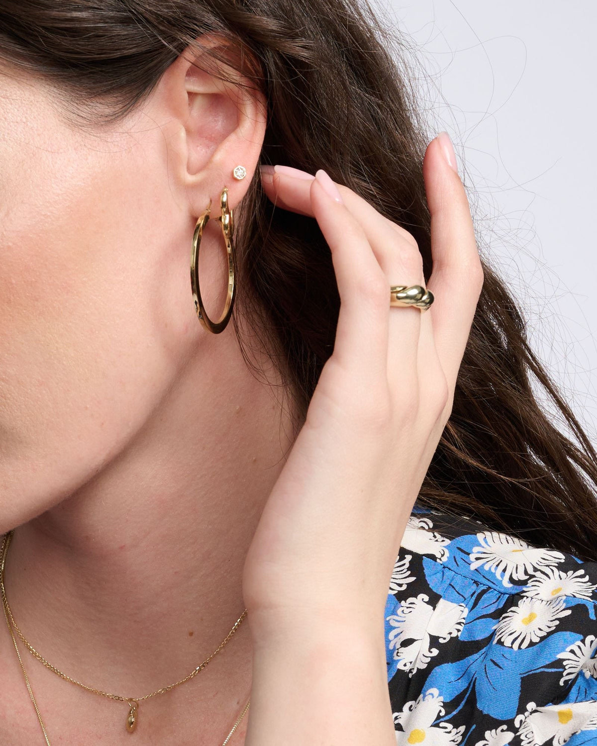 Diamond Hex Stud on the ear of a model with dark wavy hair, above a gold hoop, her hand touching her ear.