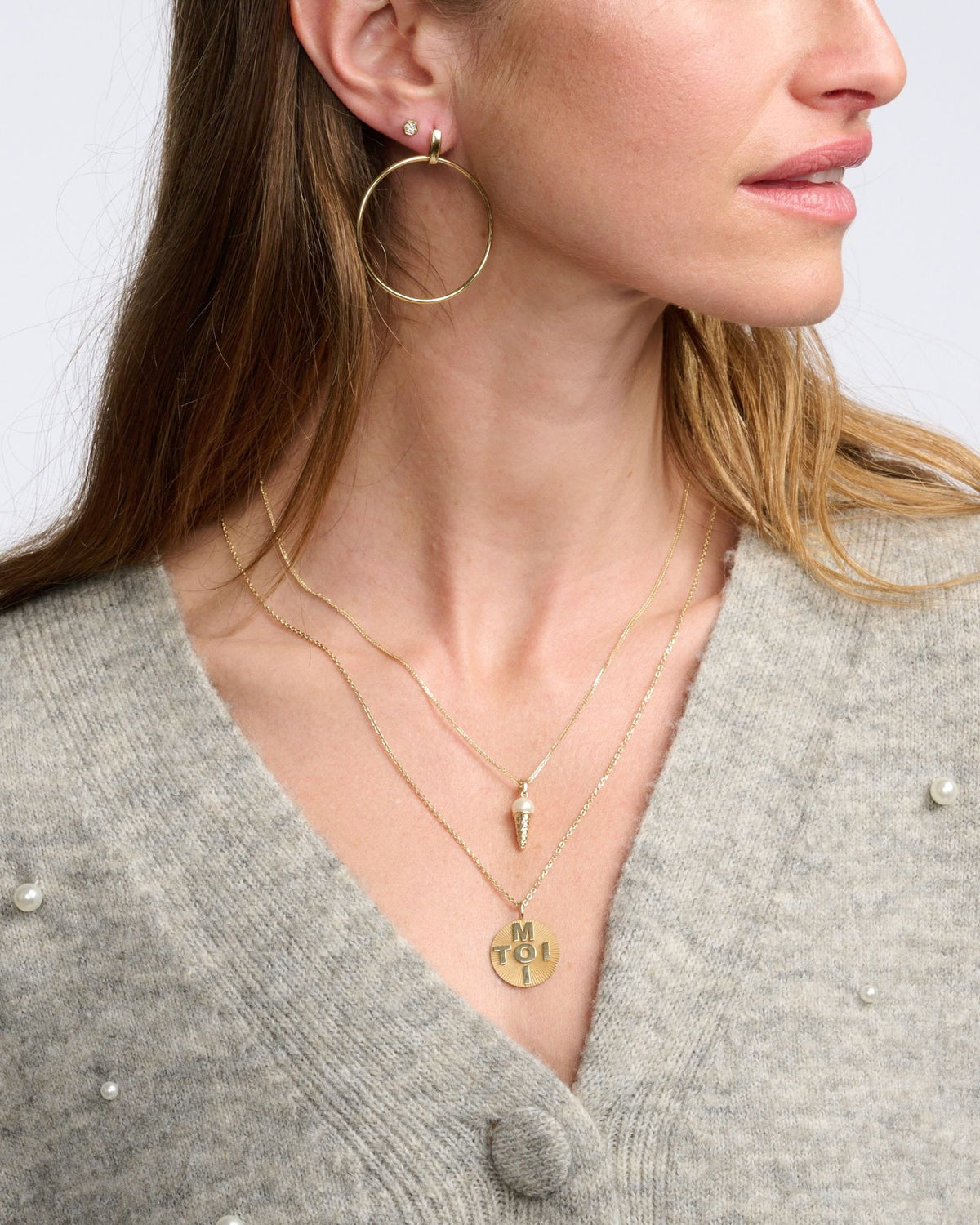 Diamond Hex Stud above a large gold hoop on a model in a grey cardigan with layered gold necklaces.