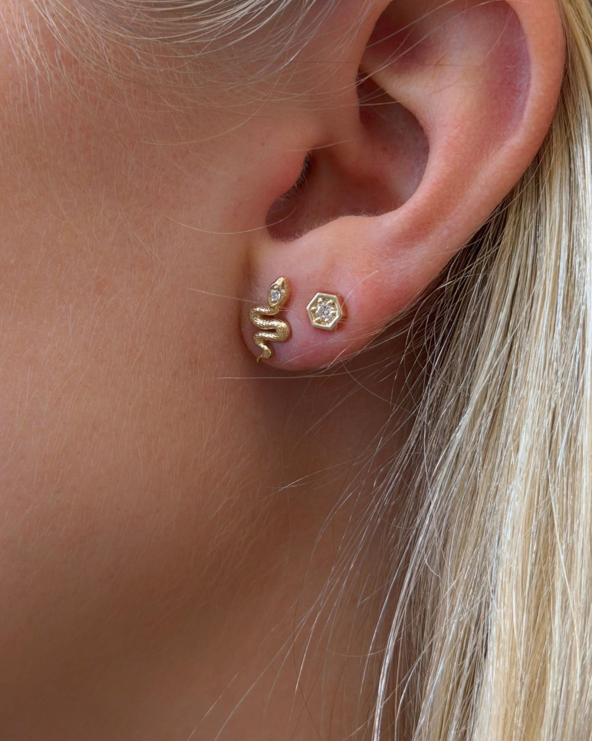 Diamond Hex Stud in close-up on the earlobe beside a gold snake stud, against blonde hair.
