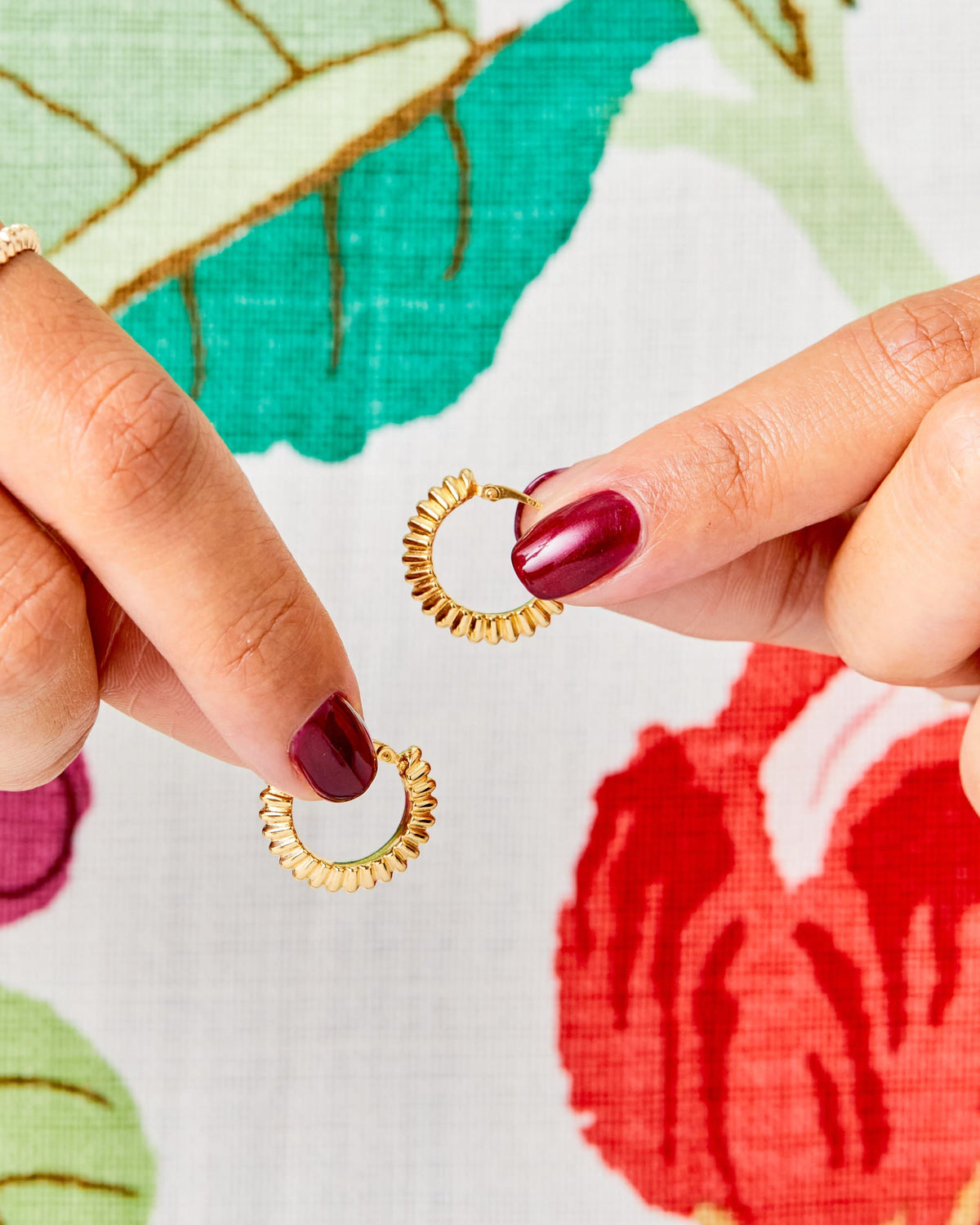 Fingers holding a Ridged Knife Edge Helium Hoop against a floral print.