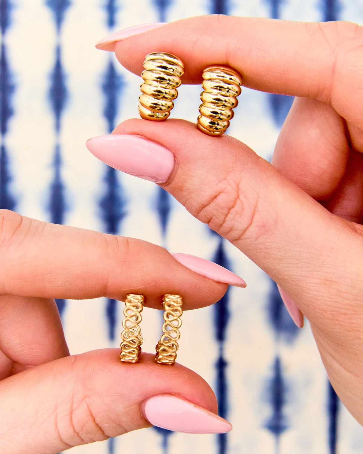 Fingers holding a pair of Lady Finger Helium Hoops against blue tie-dye.
