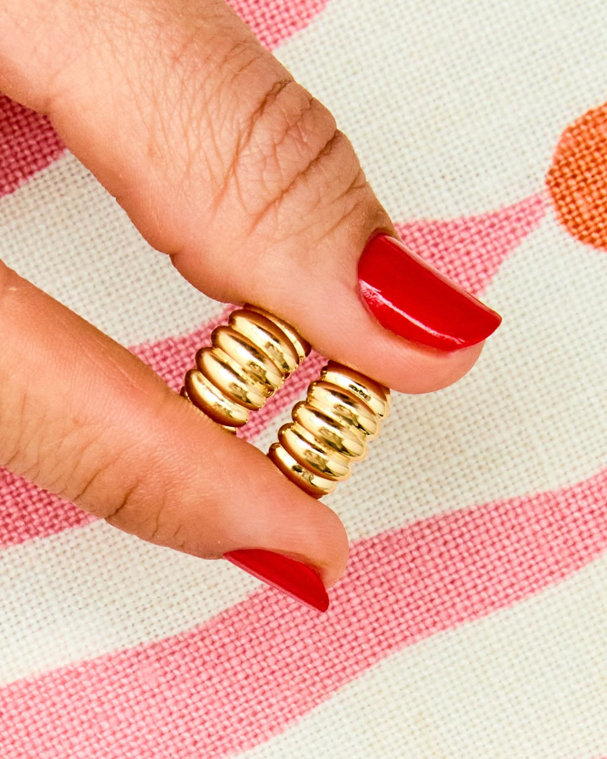 Red-nailed fingers holding Lady Finger Helium Hoops on pink stripes.