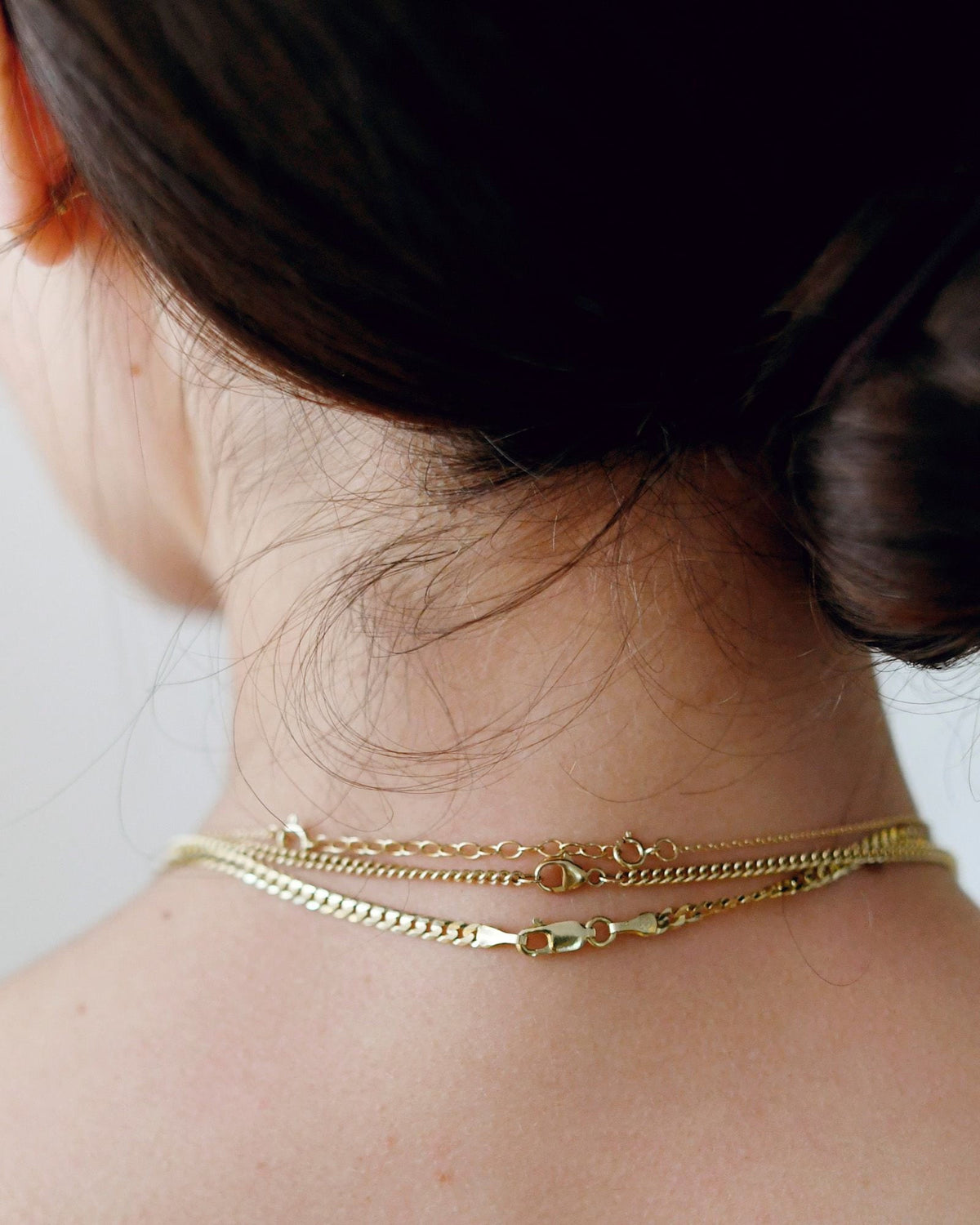 Chain Extender at the back of the neck under a low bun, with layered chains.