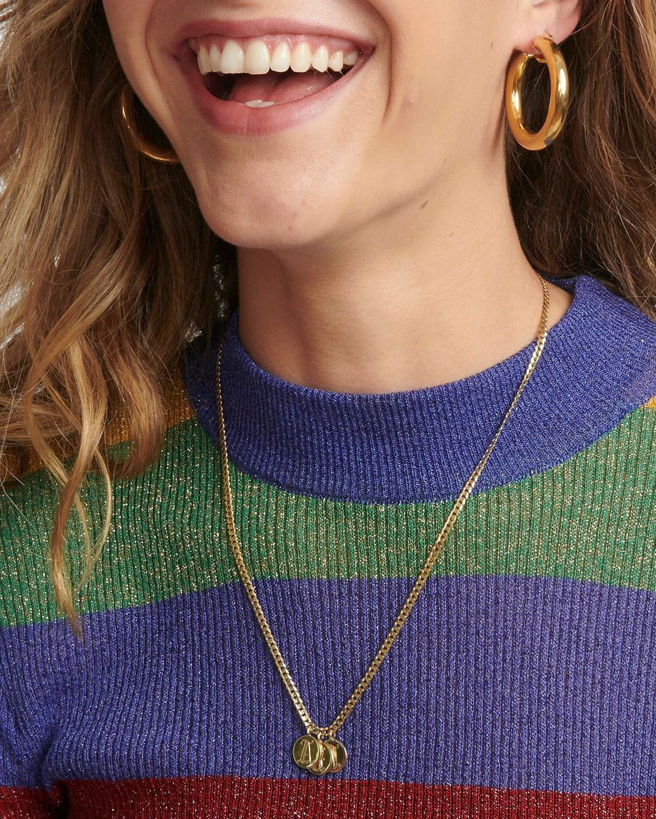 Smiling model in a striped sweater wearing a long gold Medallion Signet Necklace and gold hoops.