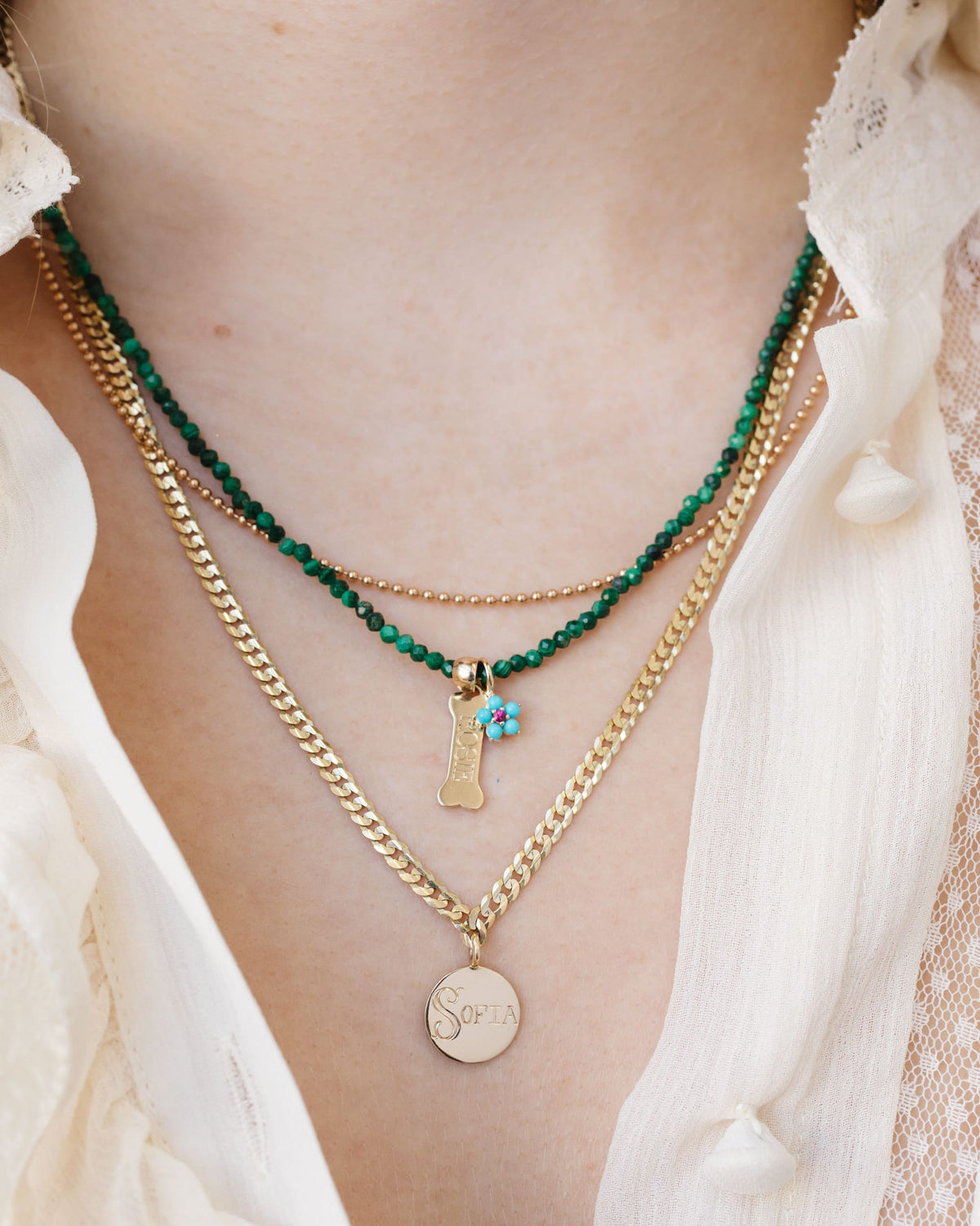 Layered necklaces on a white shirt: a malachite bead strand, a gold charm necklace and a gold Medallion Signet Necklace.