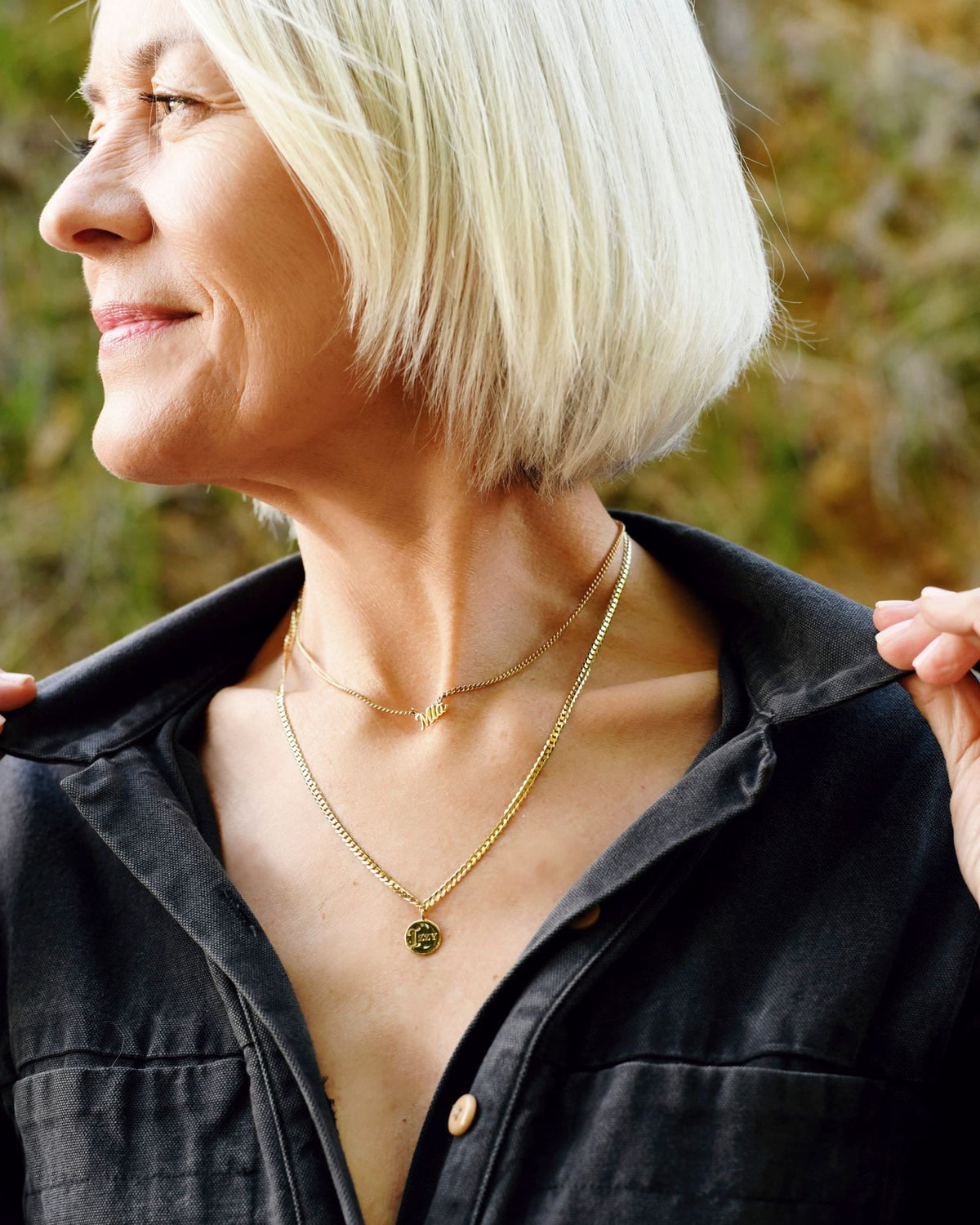 Medallion Signet Necklace layered with a beaded chain on a model in a black utility shirt, the pendant resting at her collarbone outdoors.