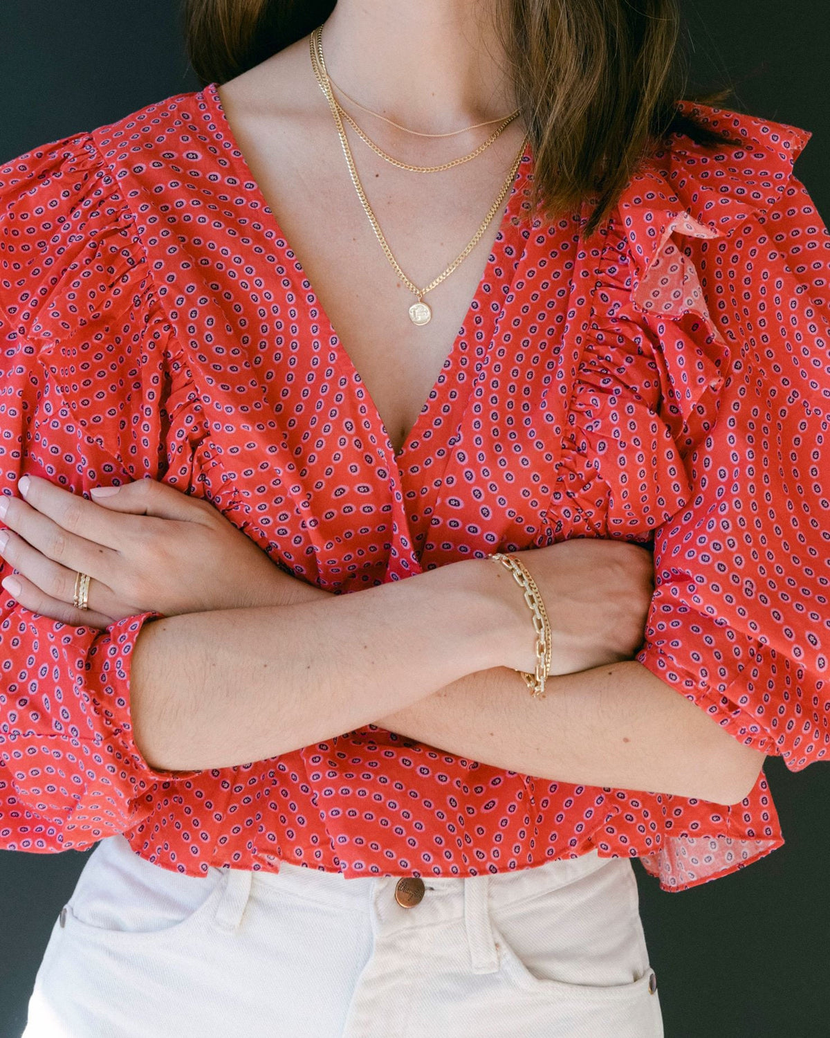 Medallion Signet Necklace layered with a dainty chain on a model in a red print blouse, her arms crossed below the pendant.