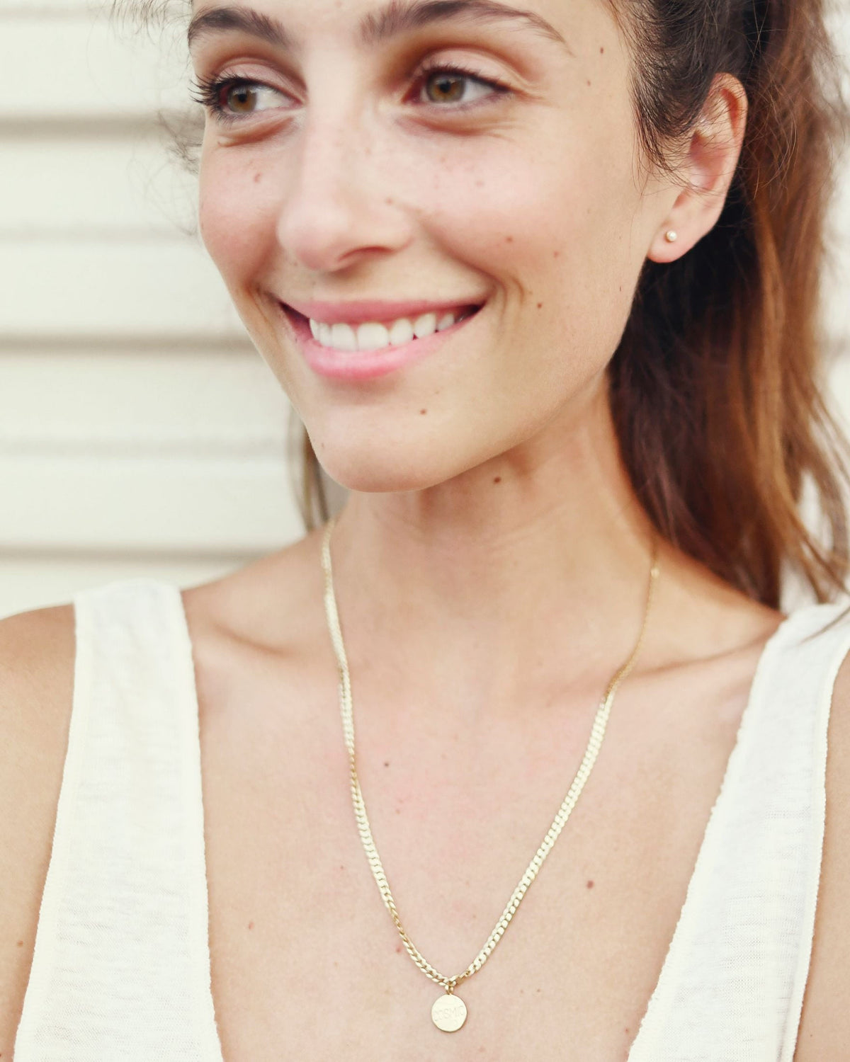 Medallion Signet Necklace on a smiling model in a cream tank top, the pendant resting on a herringbone chain at her chest.