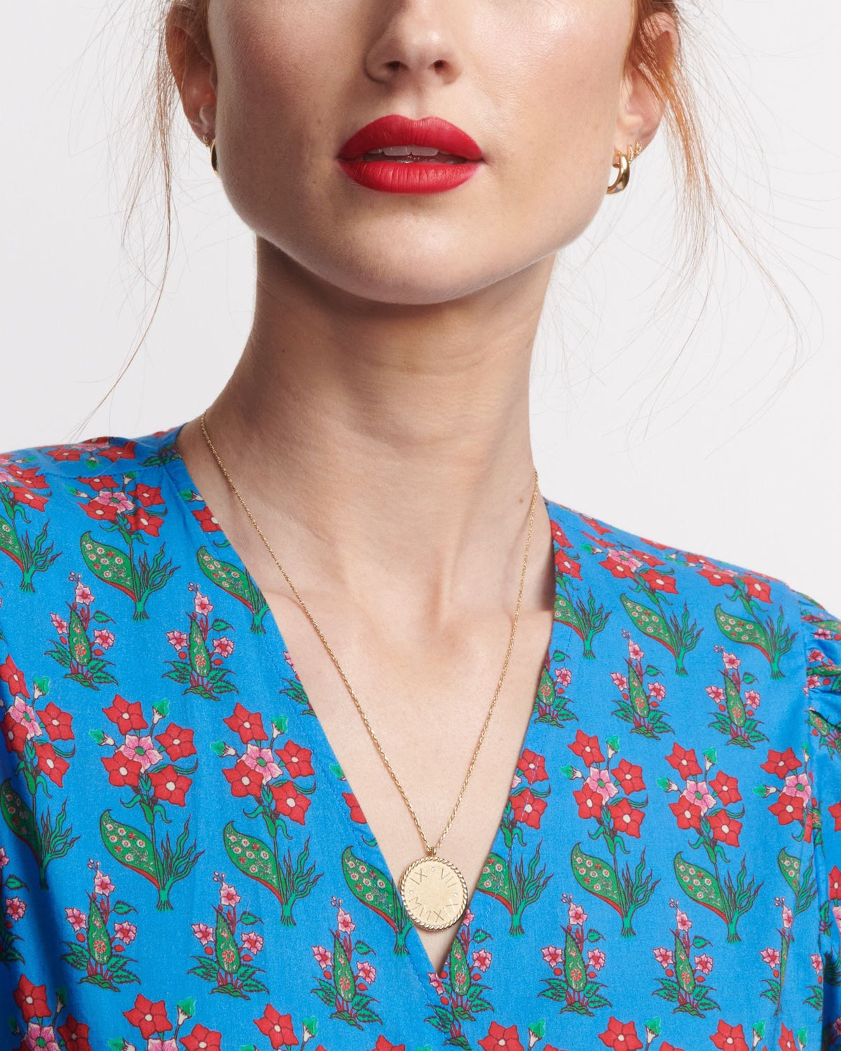 Imperial Disc Pendant on a single chain, worn against a vivid blue floral blouse with the model's chin tucked down.