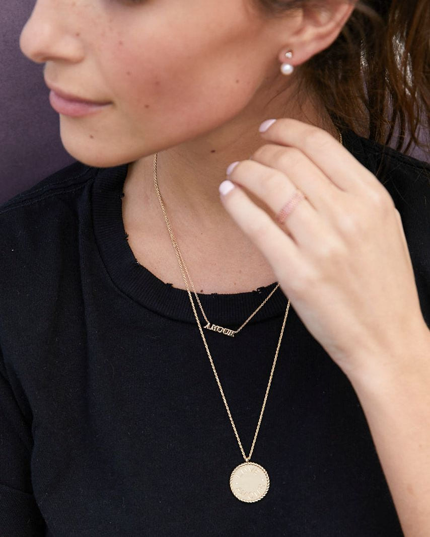 Imperial Disc Pendant engraved "amour," layered on a double chain over a black tee, the model's hand raised near her face.
