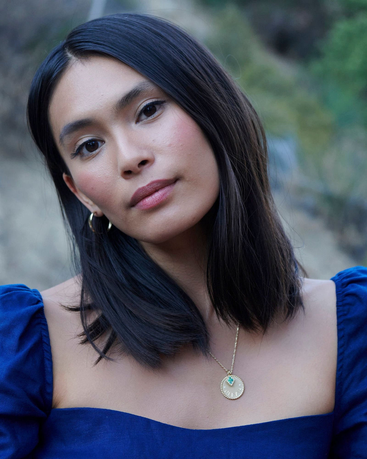Imperial Disc Pendant with a small turquoise charm, worn by a model in a royal blue off-shoulder top outdoors.
