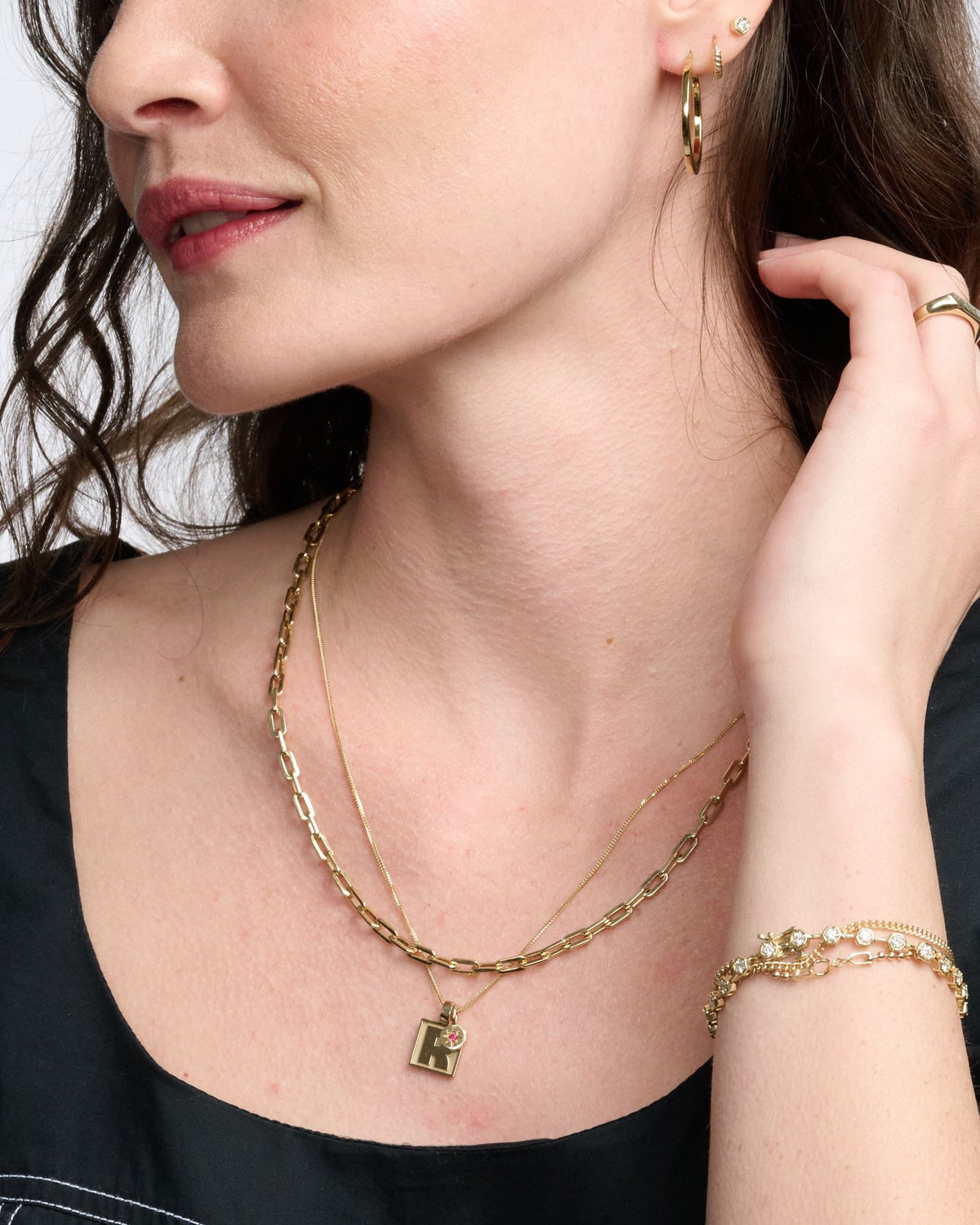 Classic Link Necklace layered with a fine chain and an initial pendant on a model in a black top, hand at her hair.
