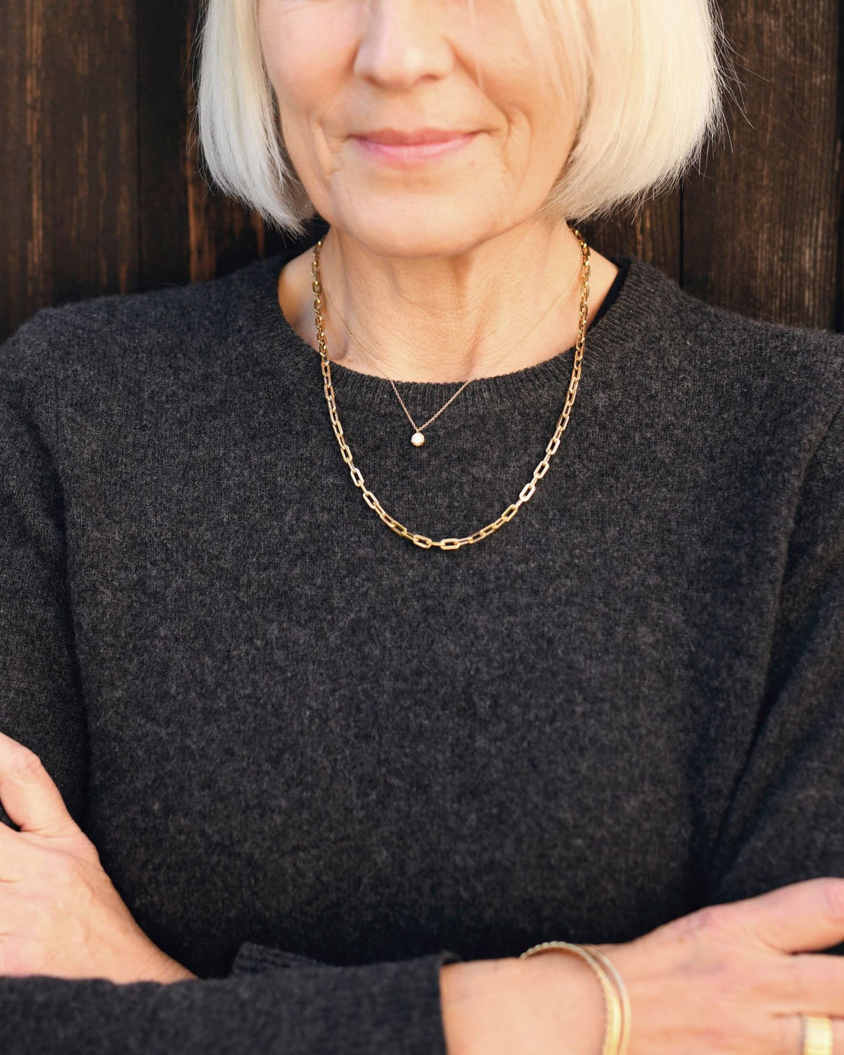 Classic Link Necklace over a charcoal sweater with a tiny diamond pendant, on a silver-haired model with arms crossed.