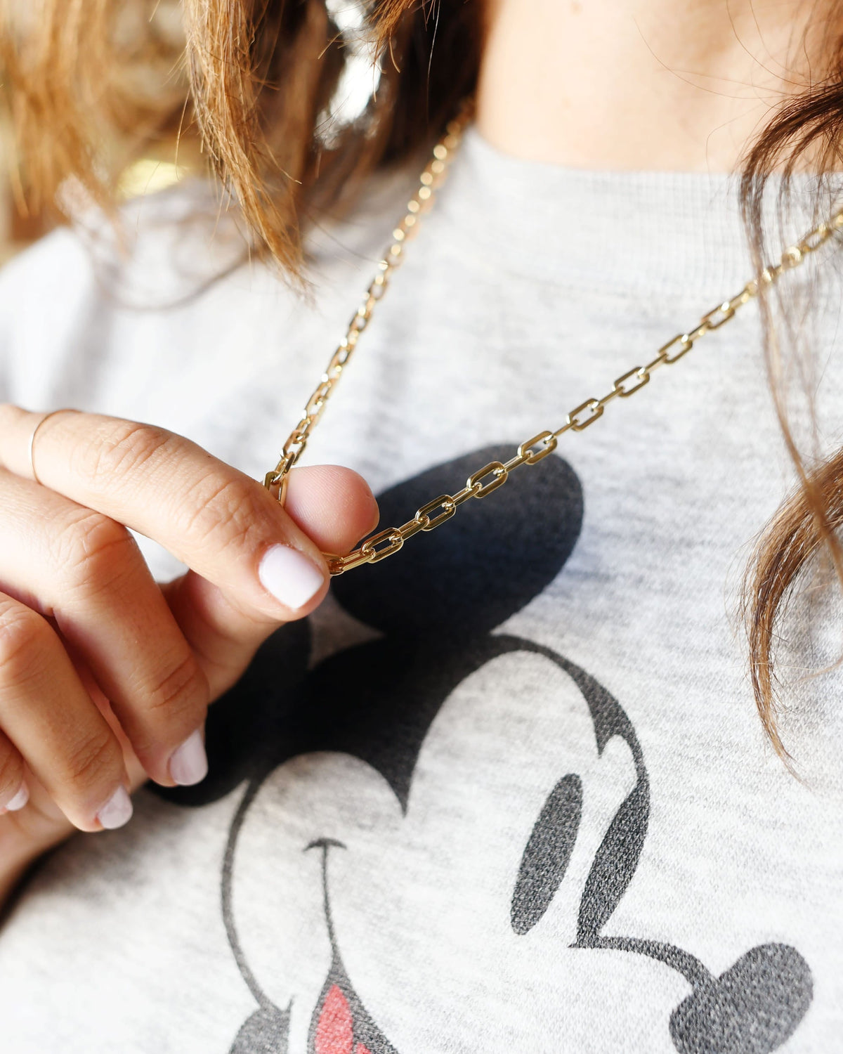 Classic Link Necklace lifted between a model's fingertips over a gray Mickey Mouse sweatshirt.