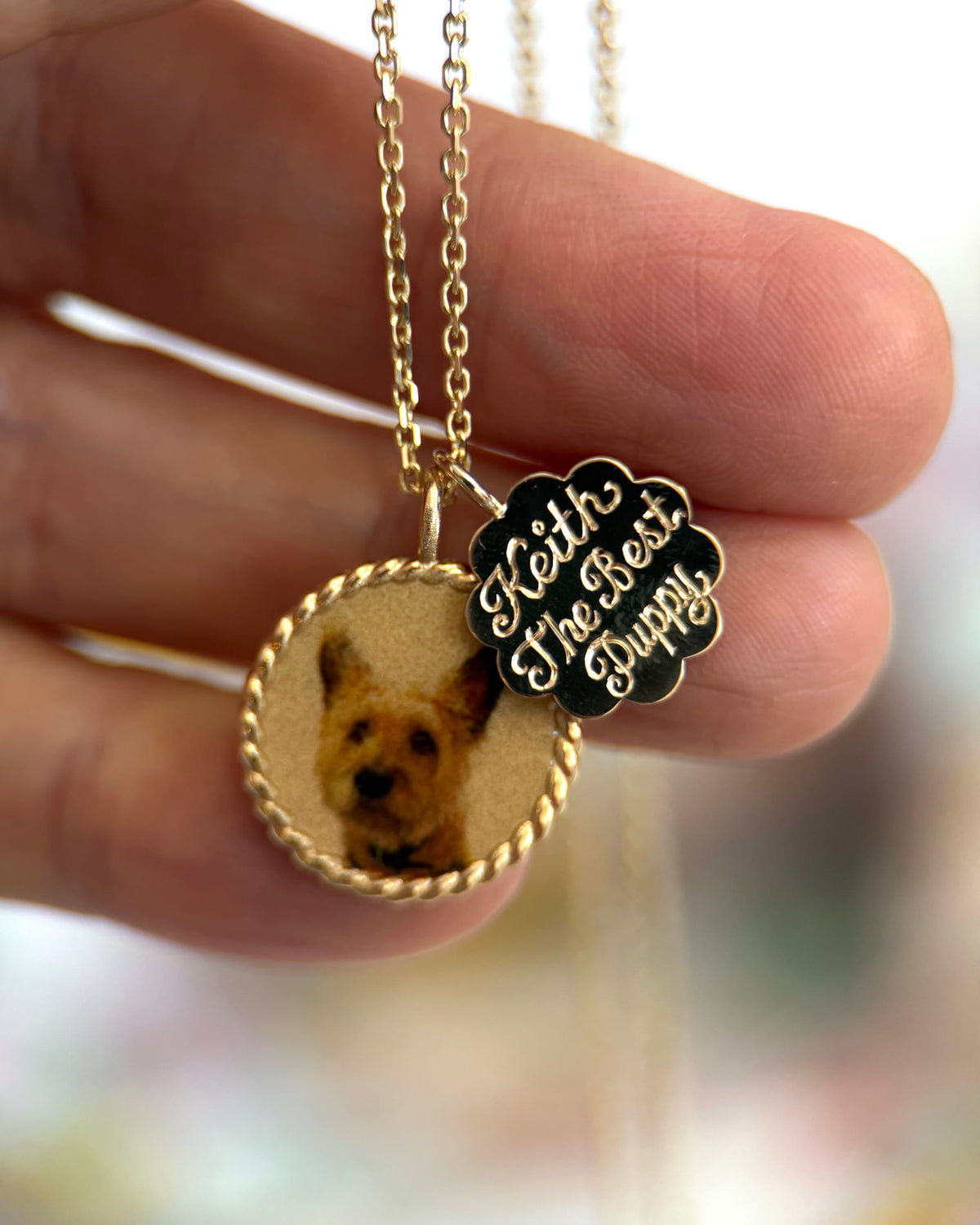 Imperial Portrait Pendant with a terrier portrait and a scalloped name charm hanging from a hand.