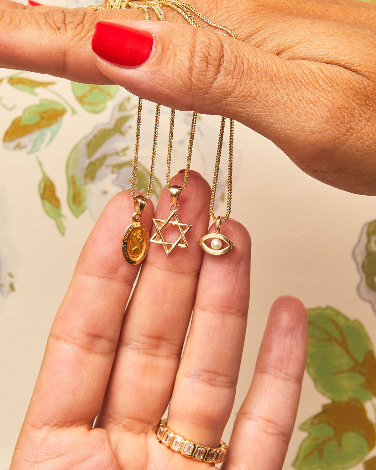 Fingers holding the Star of David, Evil Eye and St. Christopher Talisman Charms.