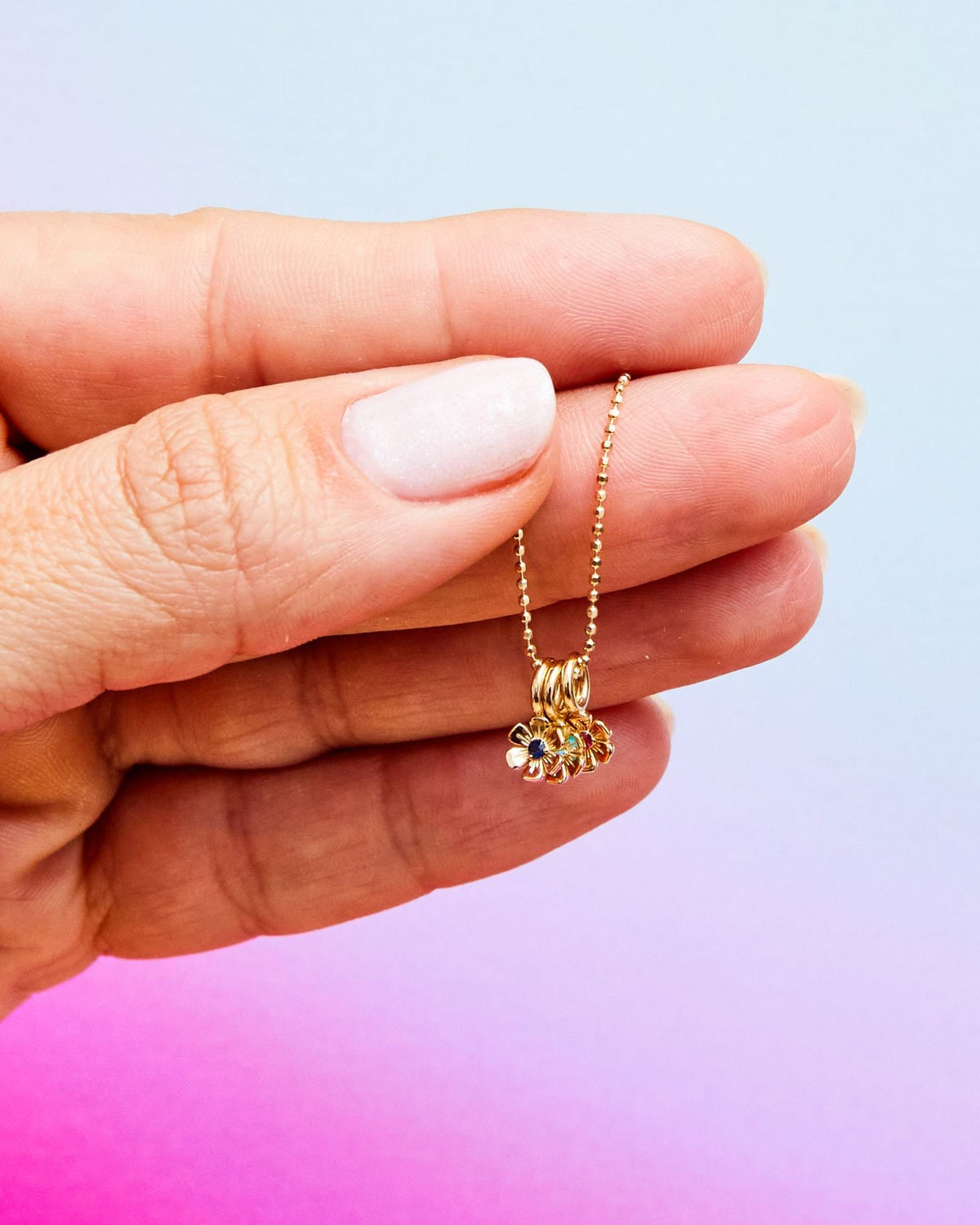 Fingers holding an In Bloom Birthstone Charm against a pastel gradient.