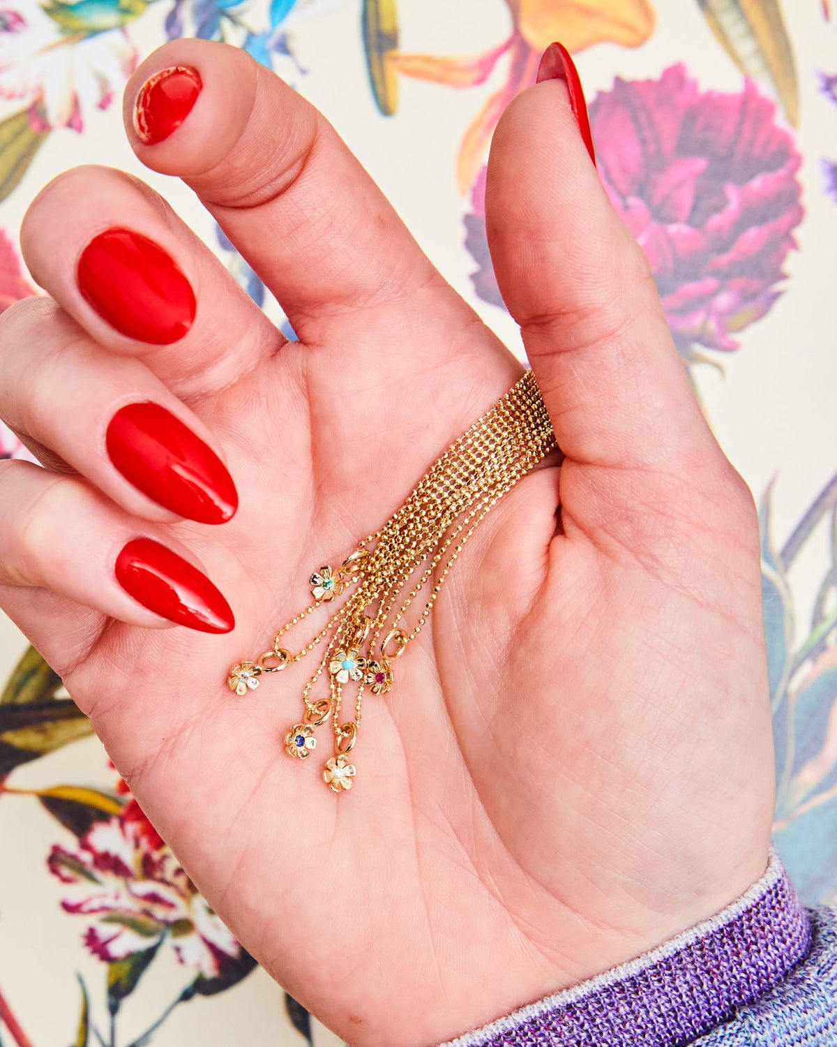 Hand with red nails holding In Bloom Birthstone Charms in several stones.