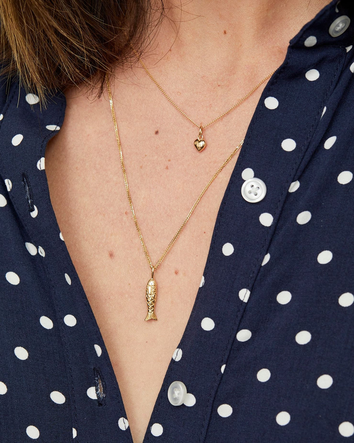 Poisson Pendant layered with a puffed heart over a navy polka dot shirt.