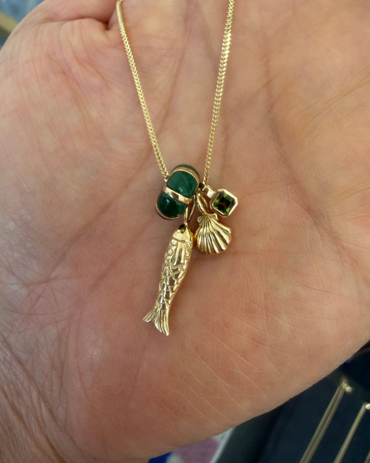 Poisson Pendant with green and shell charms in an open palm.