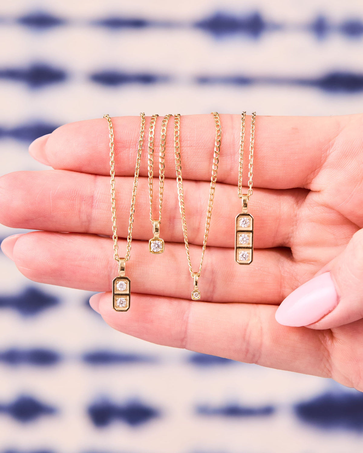 Grande Diamond Ace Pendants draped over an open hand on a blue tie-dye background.