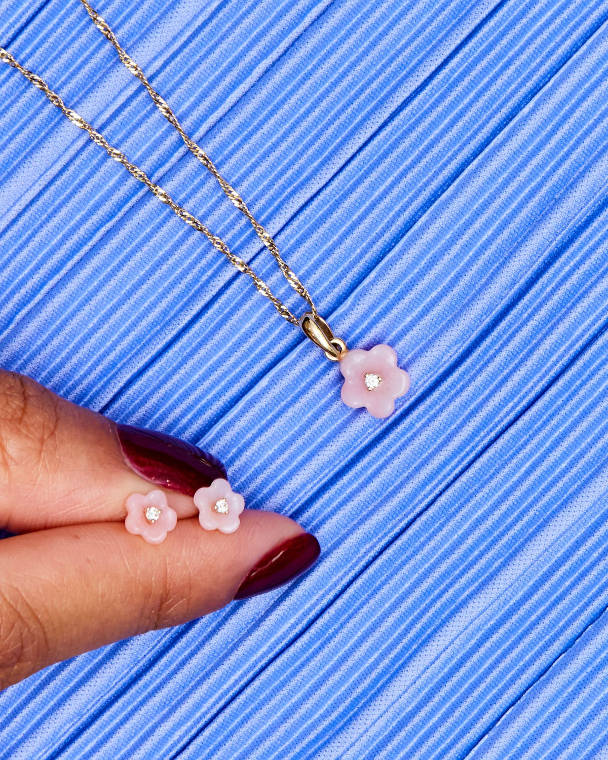 Fingers holding Diamond Blossom Peruvian Opal Charms on a blue pleated background.